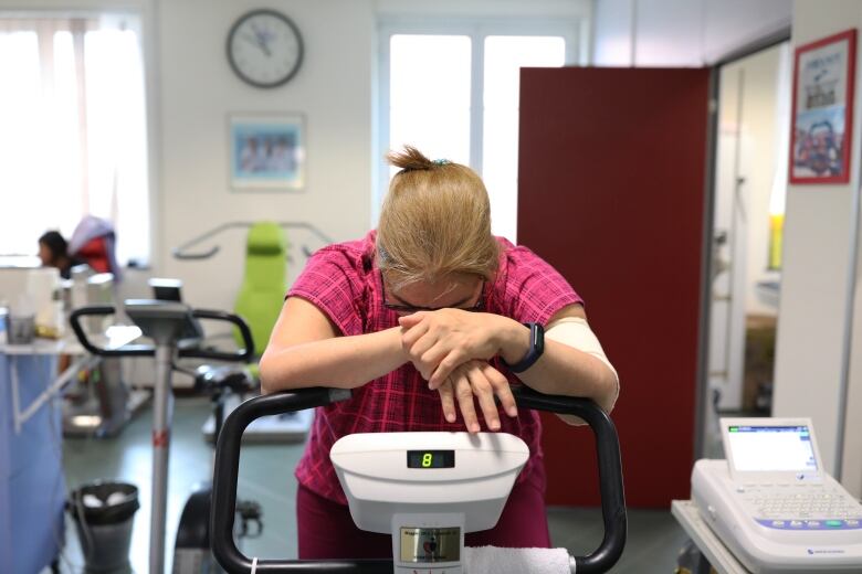 Woman rests her hands on handle bars of an exercise bike used to strengthen muscle tone for fatigue after COVID-19.