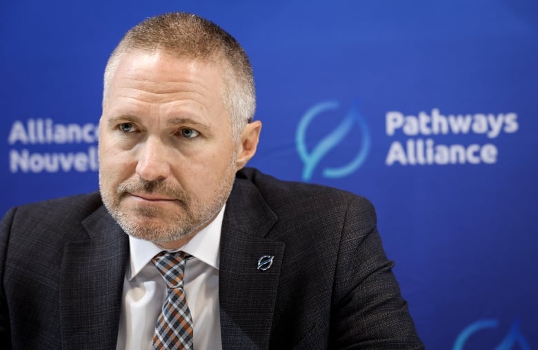 A man in a grey suit in front of a blue background