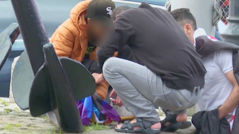 Three people crouch around a pride flag, one holding a lighter to it