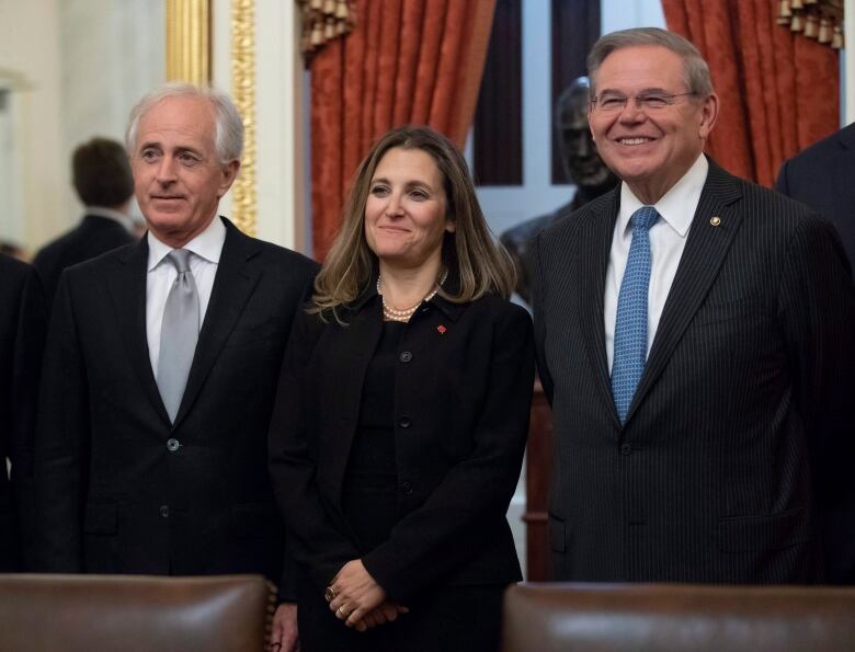 Two men in suits and ties flank a woman in professional attire.