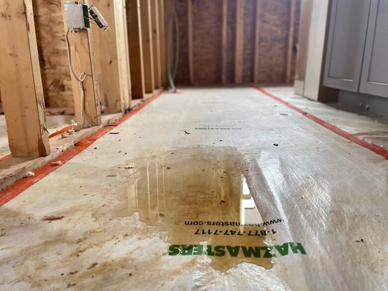 A tarp on the floor of a home is covered in muddy water. It's surrounded by exposed wooden beams.