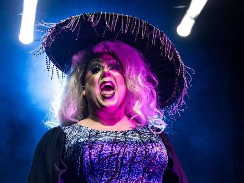 A drag performer with their mouth wide open and a wide brim hat with tassels. 