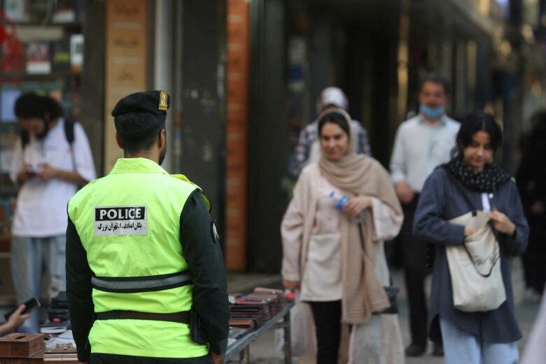 A police officer stands on a street as other people walk along it.