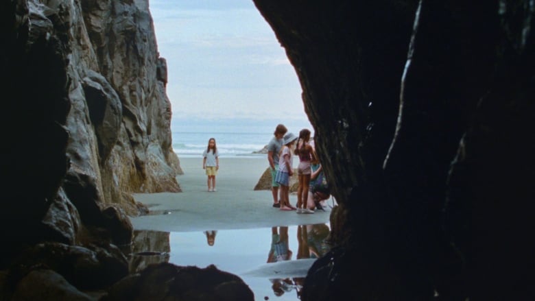 Four people are seen out on a beach from inside a cave