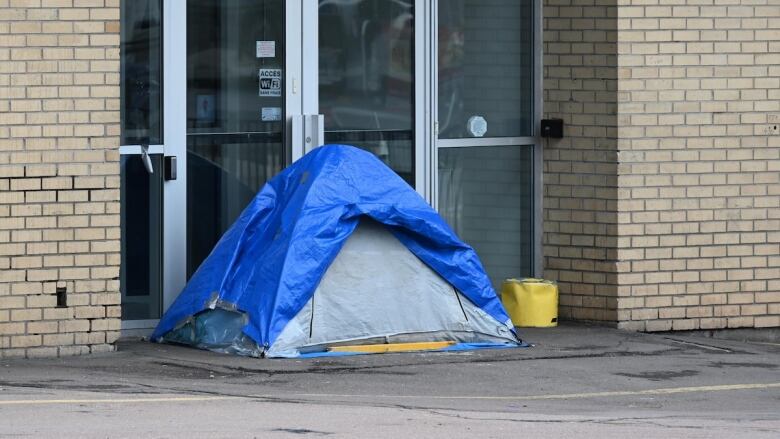 A tent covered by a blue tarp in the doorway of a pale yellow brick building.