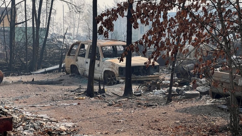 A burned vehicle and other fire-damaged debris is seen by some trees.