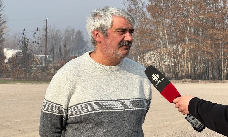 A man stands in a parking lot being interviewed by someone holding a CBC microphone.