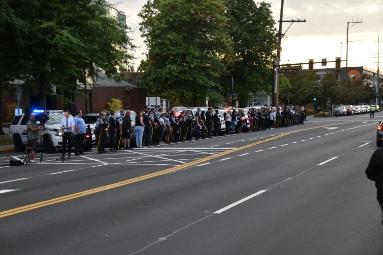 People, many in RCMP uniforms, line an empty street. 