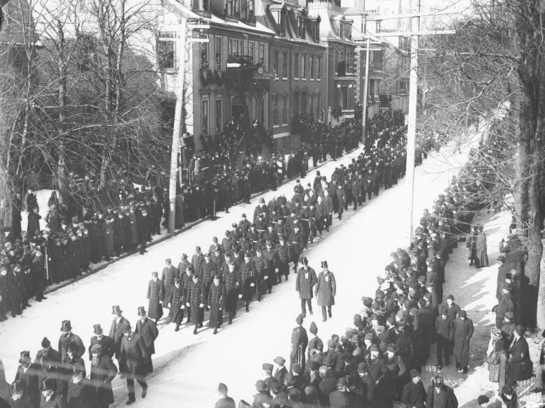 A black and white photograph of a funeral procession with thousands lining the street in black.