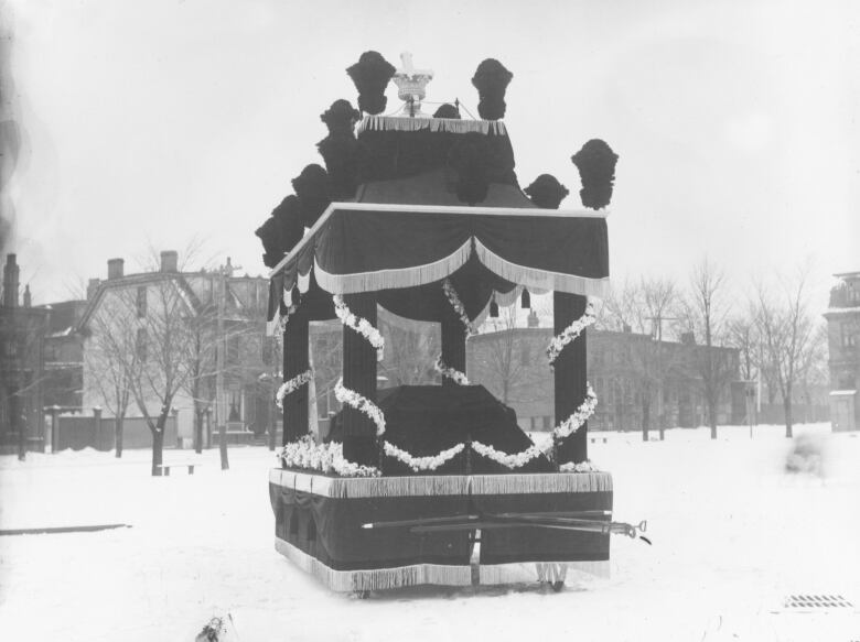 An four-poster funeral car bearing the coffin of John Thompson. It is draped in black fabric.