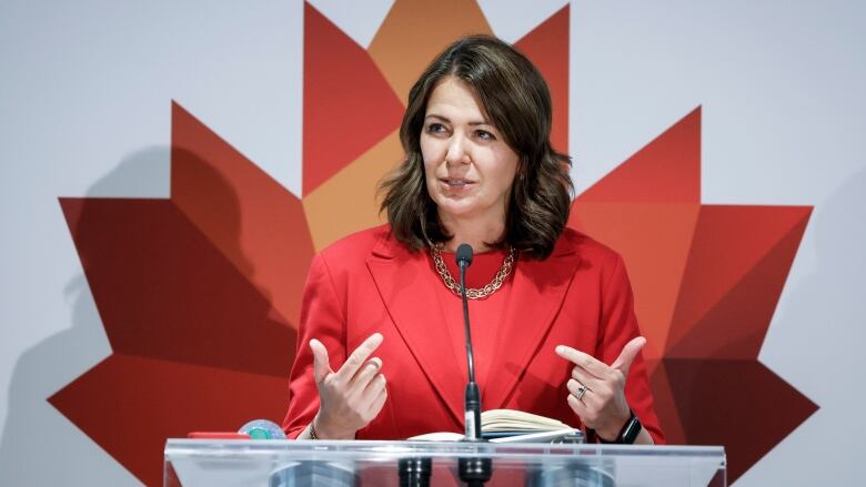 Woman speaks into a microphone in front of a large Maple Leaf symbol. 