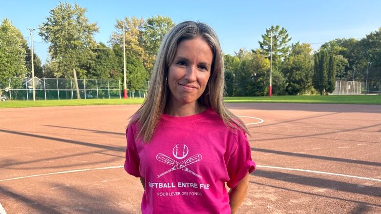 A woman in pink shirt poses for the camera on a softball pitch. 