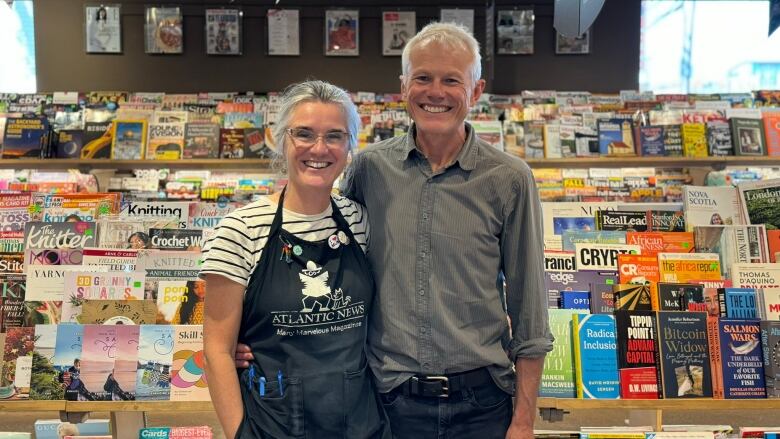 A smiling couple pose in front of a rack of magazines.