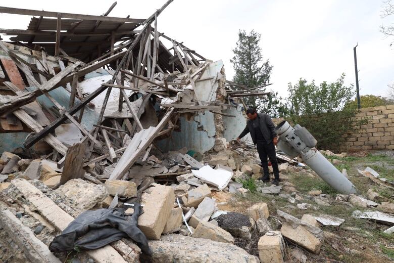 A person stands amid the rubble of a destroyed building as a missile is seen lodged in the ground.