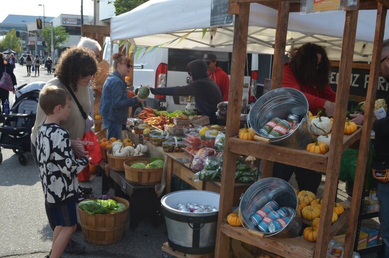 A woman and a child stand in front of a stand filled with different vegetables looking at what they should buy.