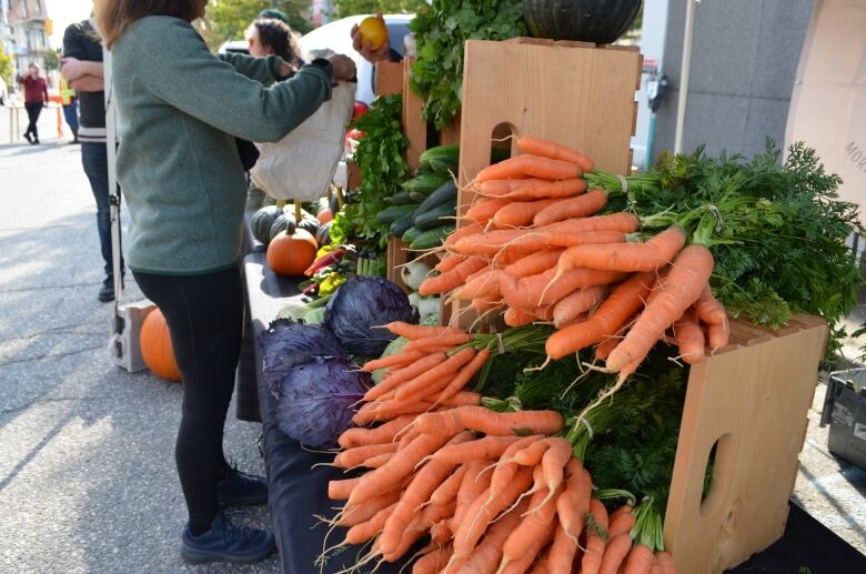 A woman has her bag open waiting for fresh vegetables, with carrots being at the forefront.