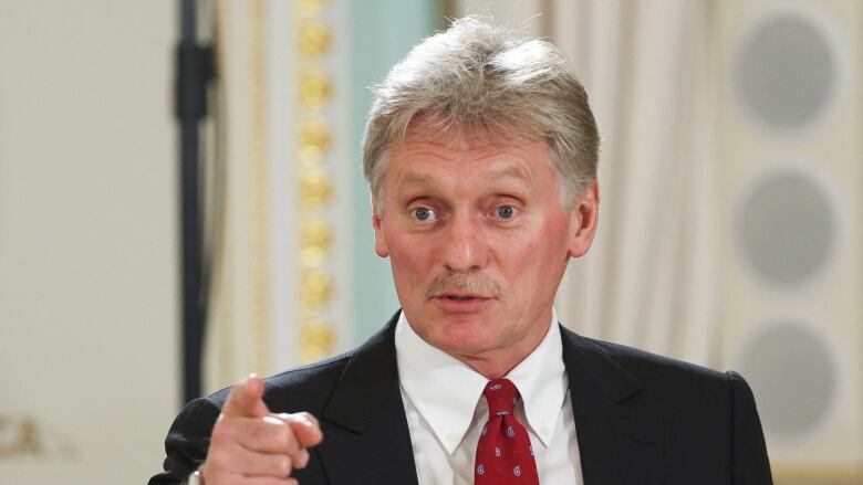 A man in a suit and tie speaks and points.