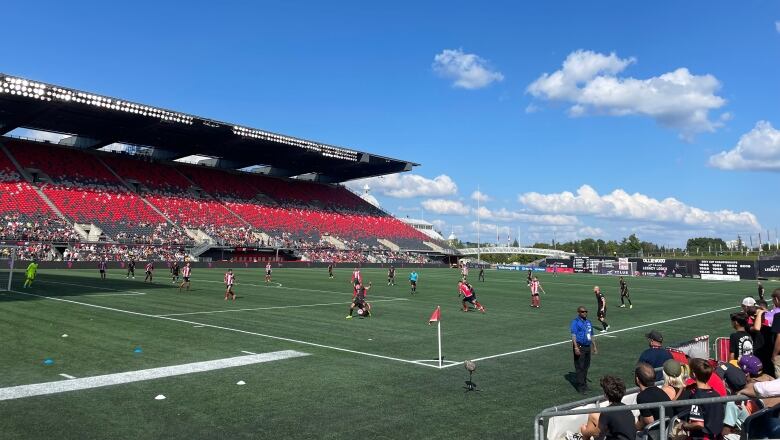 A soccer game on turf at a stadium on a sunny early autumn day.