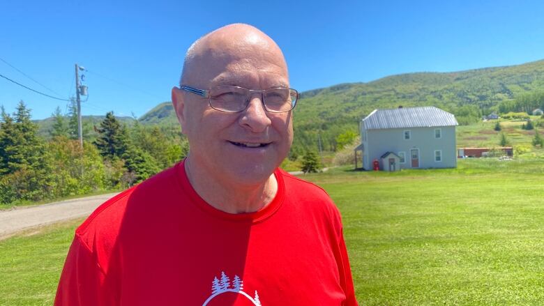 A bald man with glasses poses for the camera. He's wearing a red t-shirt. 