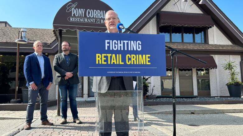 A man speaks at a podium behind a blue sign with the words 'fighting retail crime' on it.