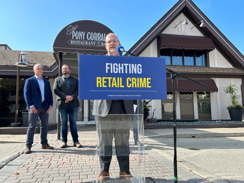 A man speaks at a podium behind a blue sign with the words 'fighting retail crime' on it.