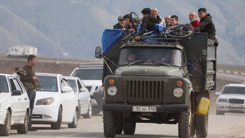 Several people are shown in the bed of a truck being driven down a road.