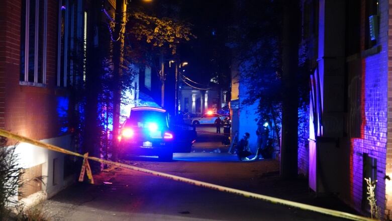 Several police cars in a taped off alleyway. 