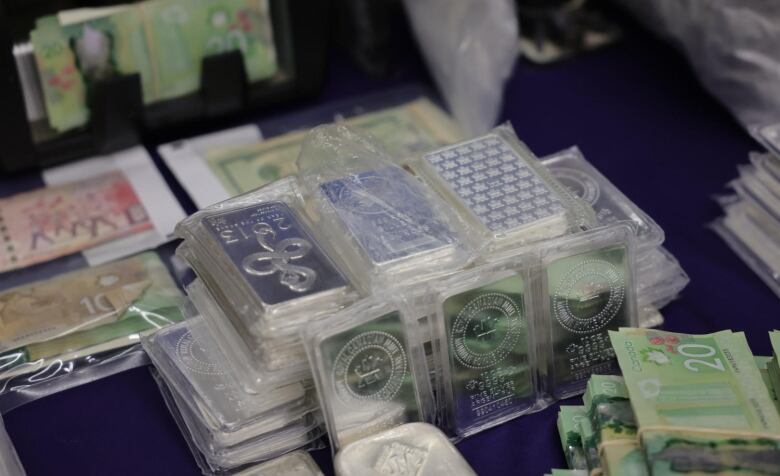 A close-up photo shows bars of silver stacked in several piles, surrounded by bundles of cash.