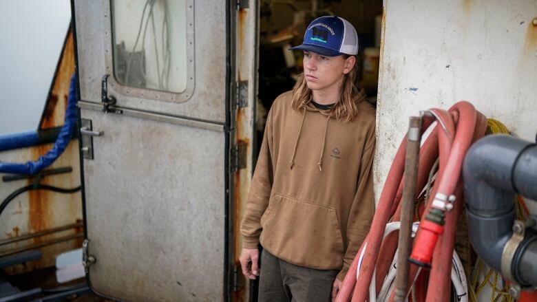 A young man stands at the cabin door on the deck of a boat.