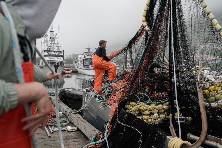 A man climbs among some fishing nets on a boat docked in a marina.