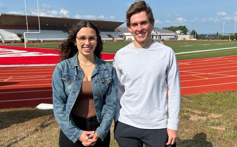 A brother and sister standing near a sport field 