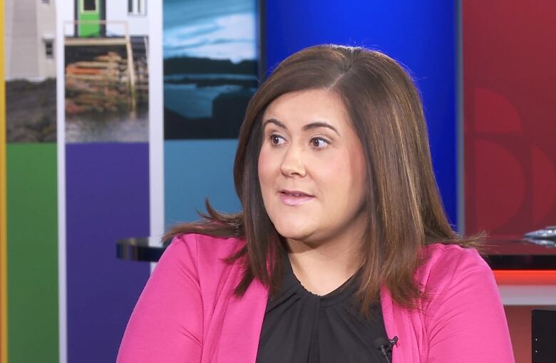 A woman sits wearing a bright pink blazer.