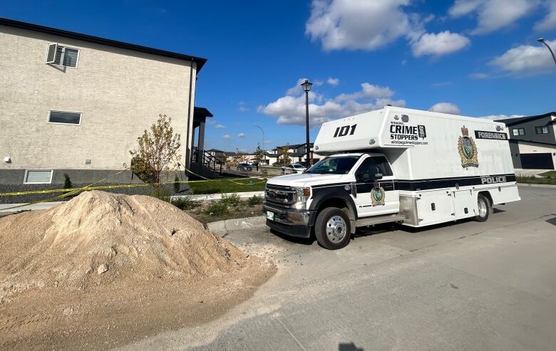 A large white camper-style van with black stripes and police and crime stoppers decals is pictured parked outside a two-storey duplex in a residential neighbourhood.