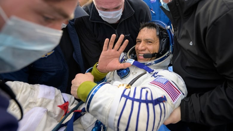 An astronaut waves as he is helped out of a space capsule after returning to Earth from the International Space Station.