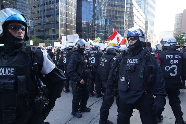 Riot police stand in the street, with a Canadian flag seen behind them.