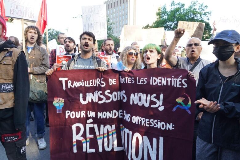 Protesters hold a sign saying workers of all kinds come together for a world without oppression: Revolution! in French.