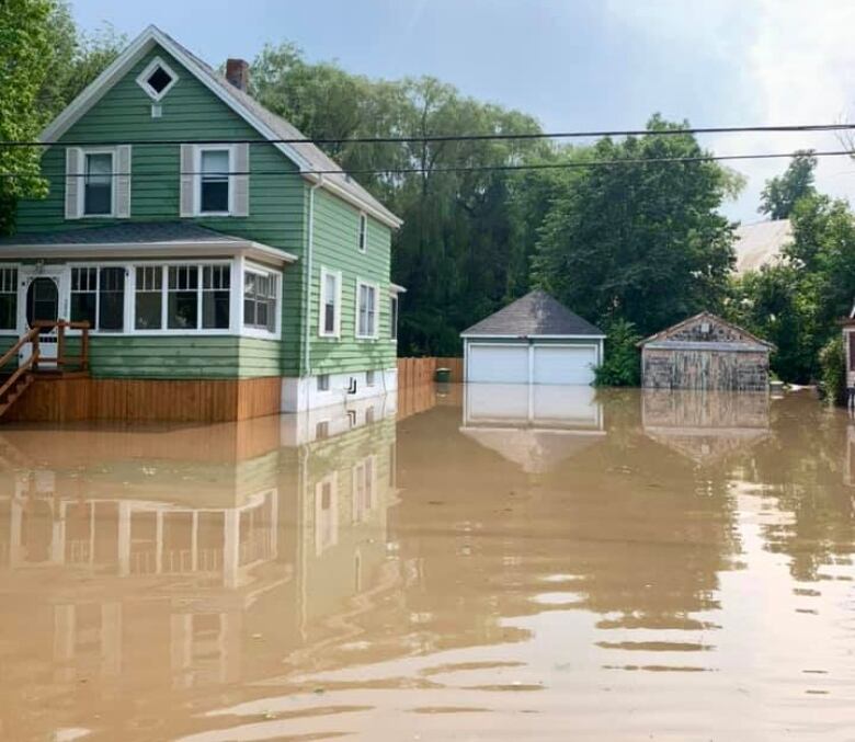 A green house is surrounded by flooding. It's all brown water that surrounds the home. 