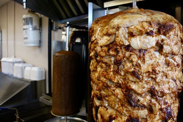 A closeup of sizzling chicken stacked on a rotating spit.