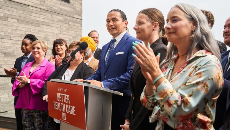 A man surrounded by several other people speaks at a podium.