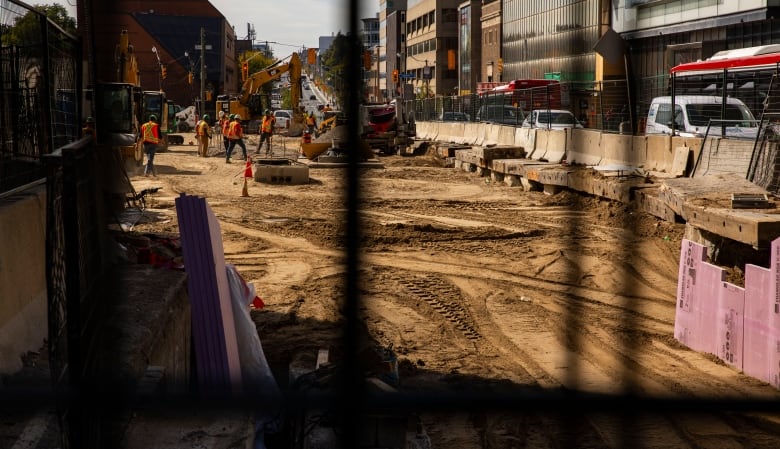 Construction workers work on a construction site in a city. Cars and buses are seen in the background on the road. 