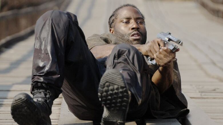 A man lying on his back holds up a futuristic pistol. He points it out of frame. 