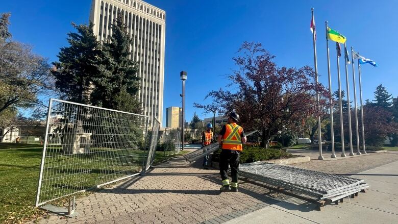 Two men wearing orange safety vests dismantle the fencing around Regina city hall. 