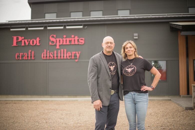 A man and a woman stand in front of a distillery.