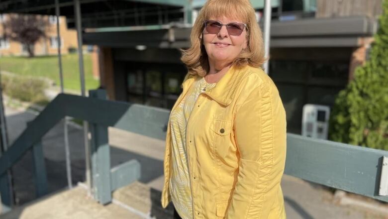 blonde woman in yellow shirt, yellow jacket and sunglasses smiling at the camera