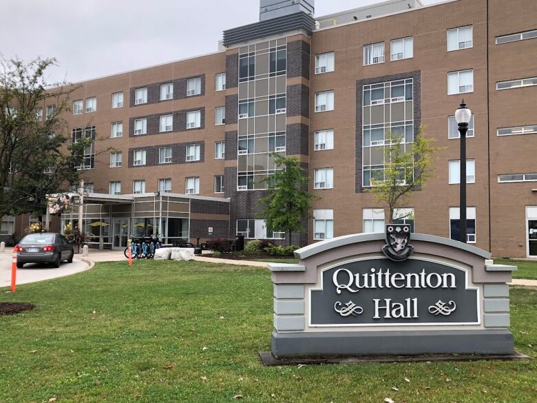 A photo of a sign with a student dorm in the background. 