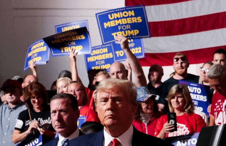 People hold signs like 'Union Members For Trump' behind Trump.