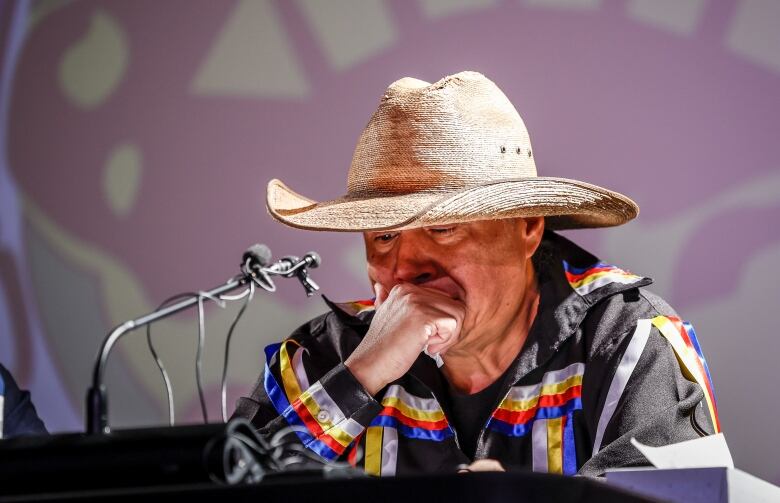 A man speaking at a press conference appears emotional as he looks down at the table.