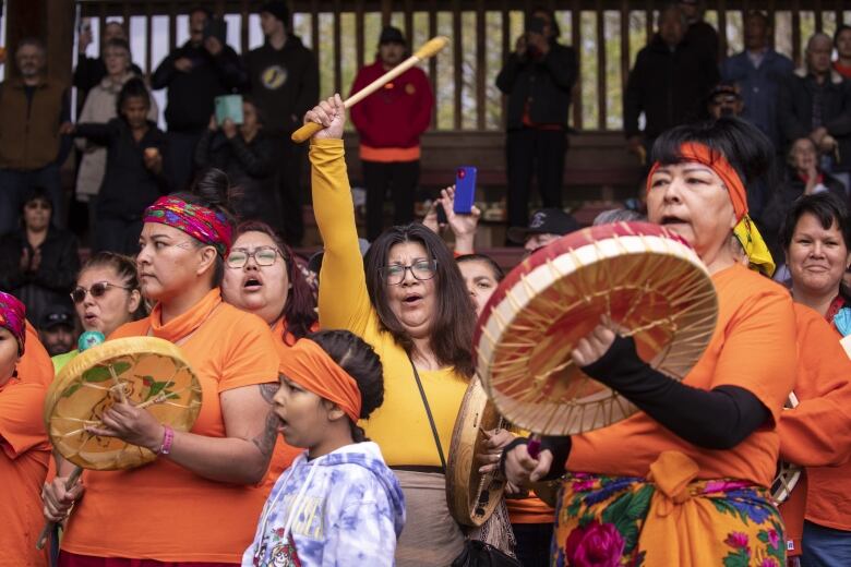 A group of people in orange shirts and pictured singing with drums. 