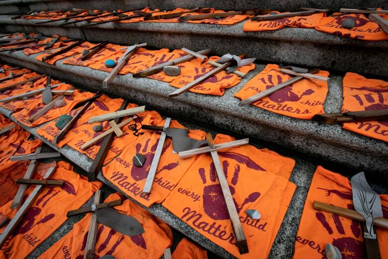 Orange shirts are folded and placed on steps with crosses placed on top. 