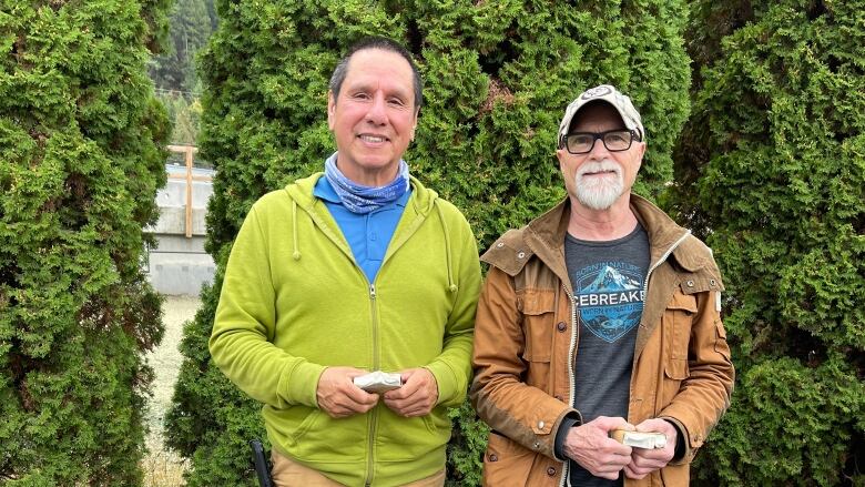 Two men stand side by side smiling in a parking lot. 